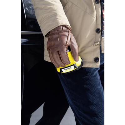 A person is wearing brown gloves and holding a yellow device with the 'Kärcher' logo next to a black car.