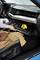A person opens the glove compartment of a car and reaches for a yellow object inside. A coat is lying on the seat.