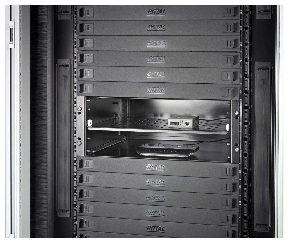 A server room with several black servers in a rack. One bay is empty, with the shelf below showing some cables and a small device.