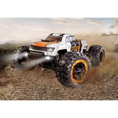 A remote-controlled monster truck model with large tyres drives over a dusty path, kicking up dirt.