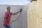 A person is spraying paint onto an outdoor wooden fence using a paint spray gun. They are wearing a protective mask.