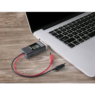 A laptop on a wooden table with a connected voltage meter checking the voltage over USB.