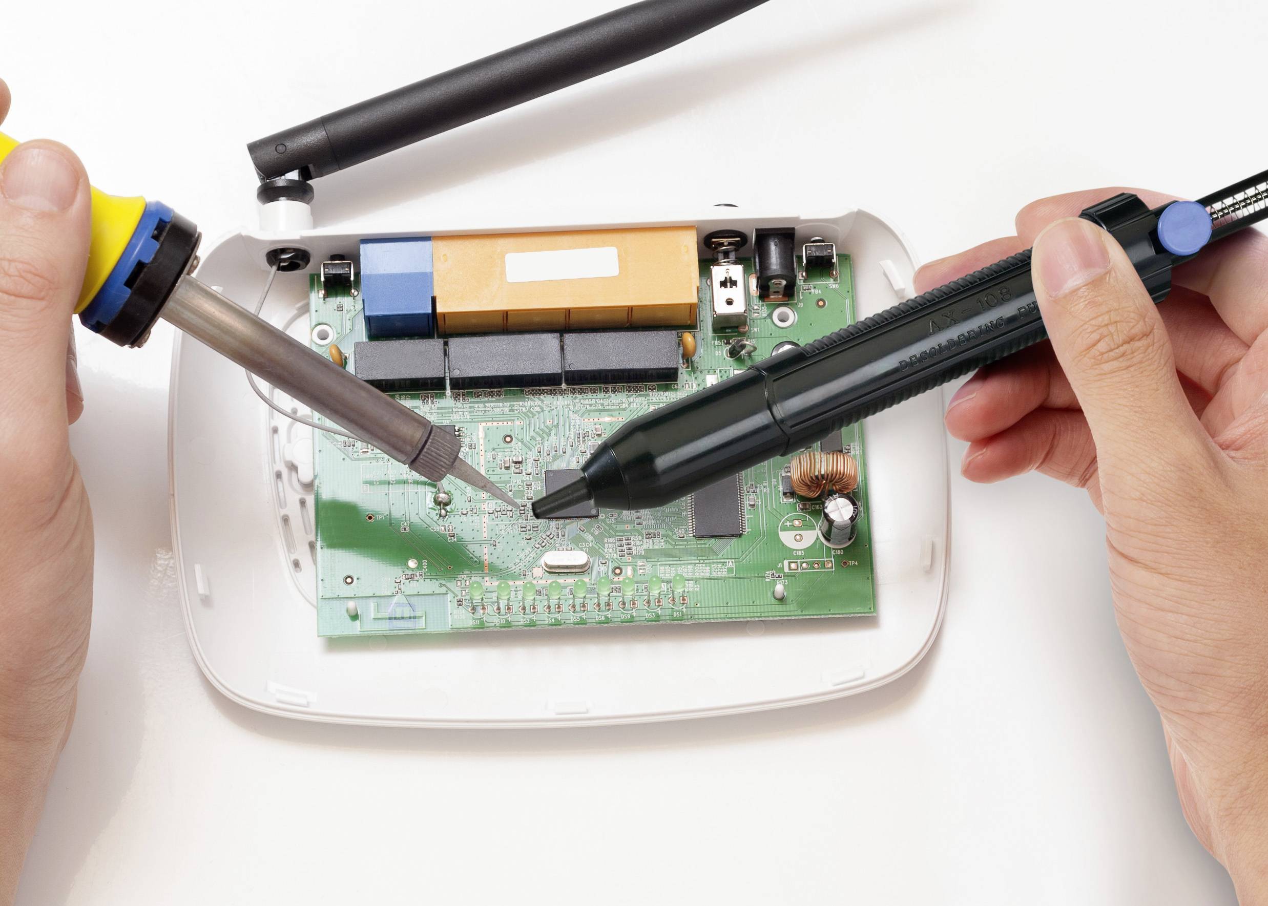 'A person solders an electronic circuit board using a soldering iron and solder suction pump.'