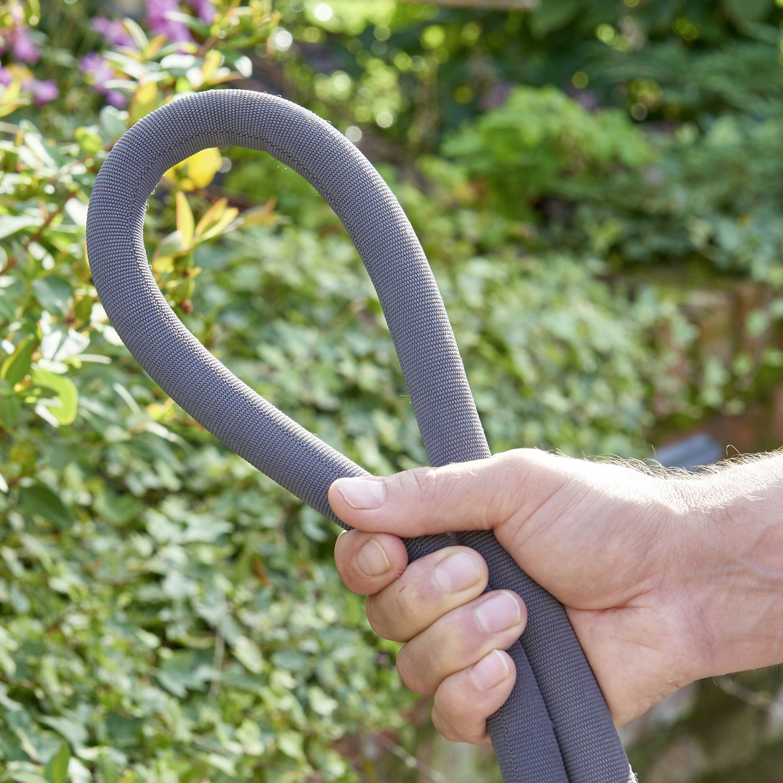 A hand is holding a grey garden hose section in a blooming garden.