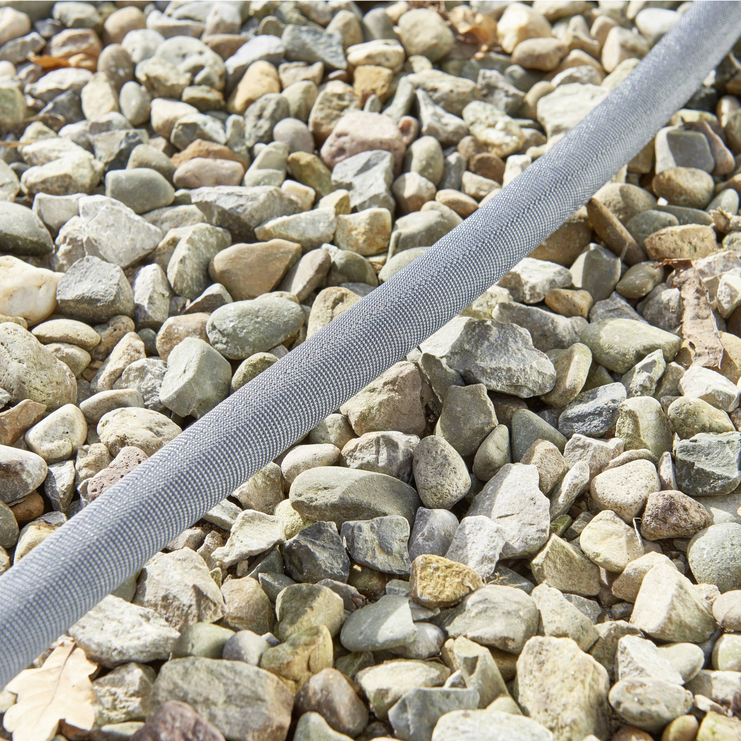 A grey water hose runs diagonally across a surface covered with pebbles. The focus is on the texture of the hose.