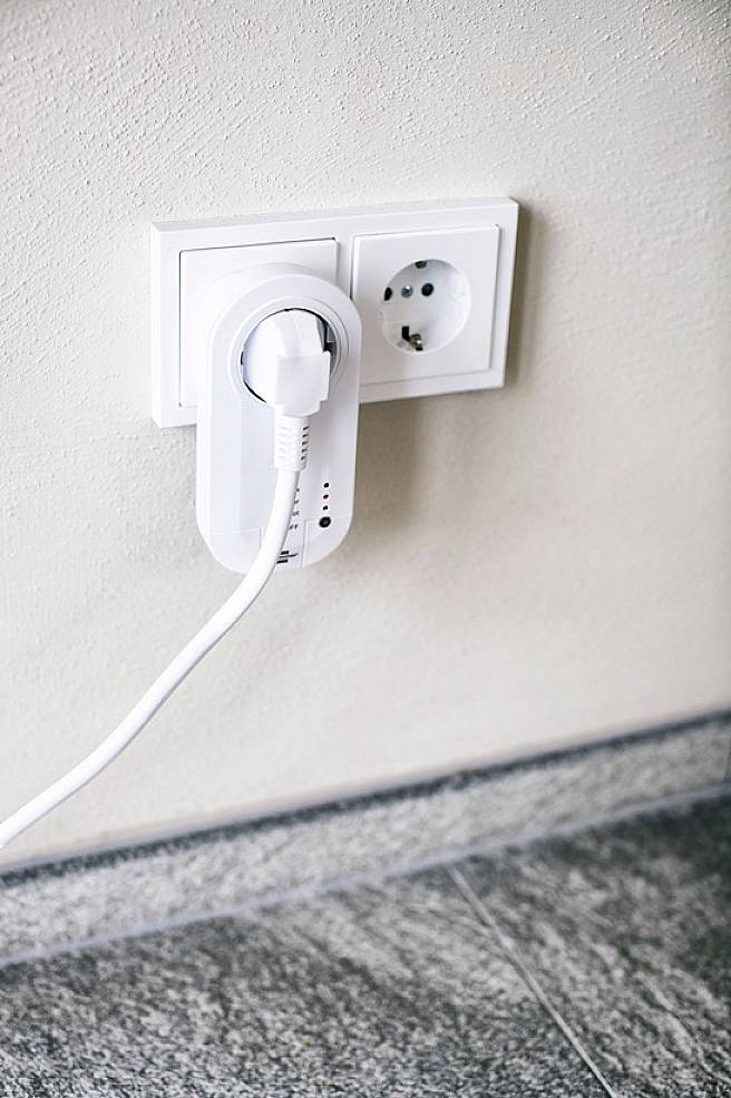 'A white plug adapter is plugged into a wall socket. A cable leads away from the adapter.'