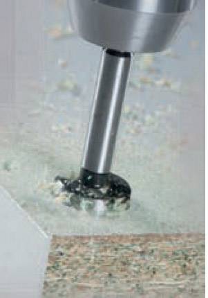 Drill working on the surface of a wooden board. Drilling shavings surround the drill site.