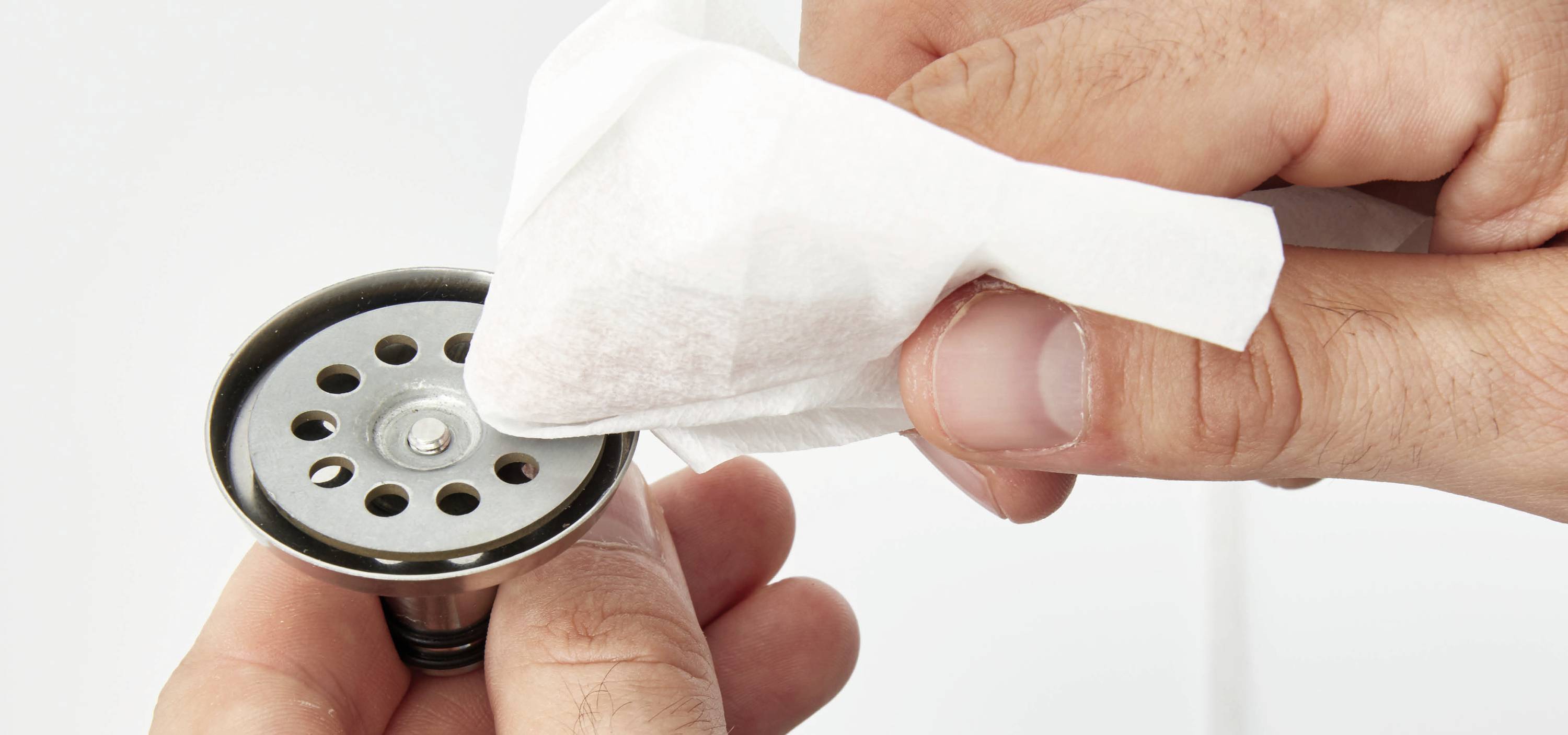 Two hands are cleaning a water drainage point with a white paper towel.