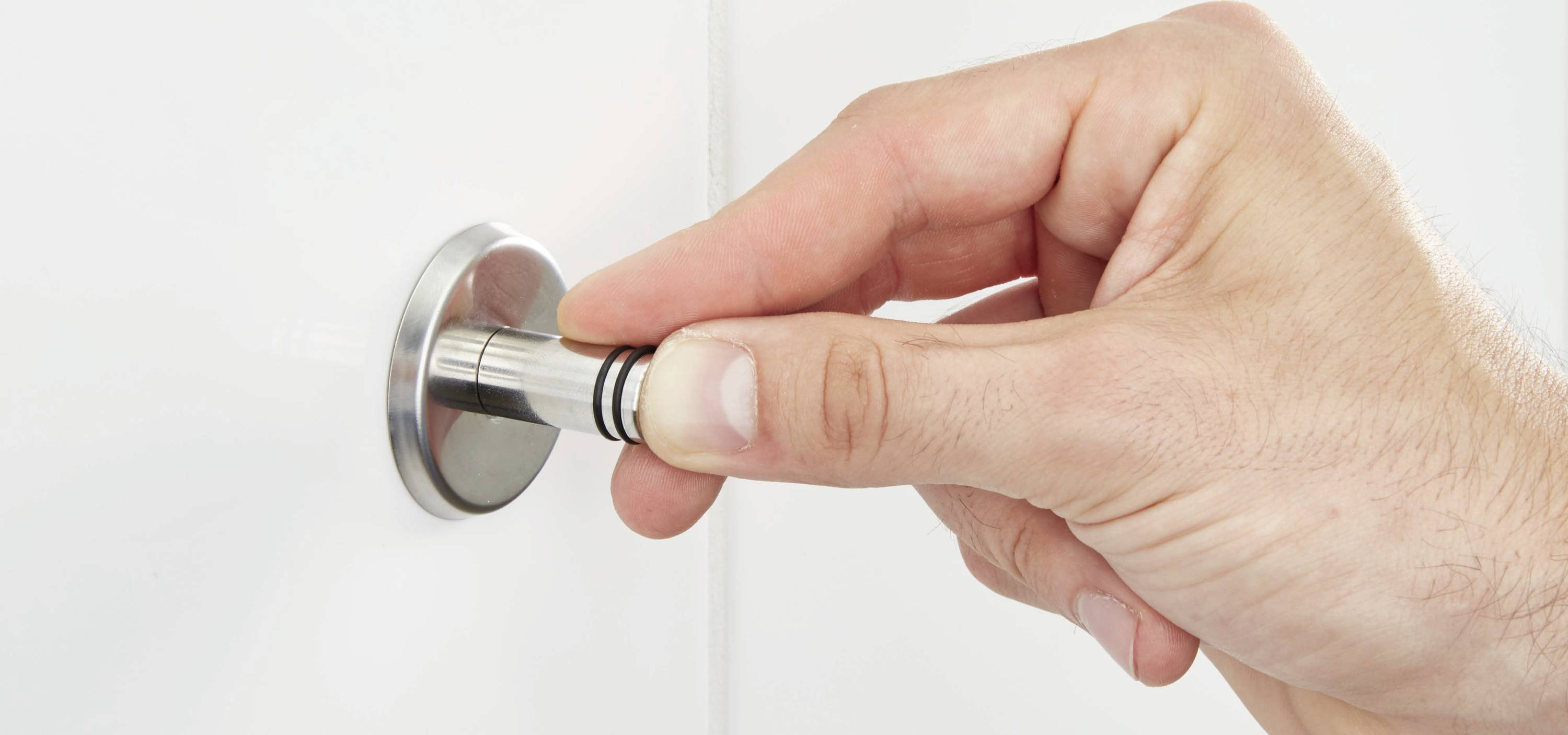A hand is turning a round door handle on a white door.