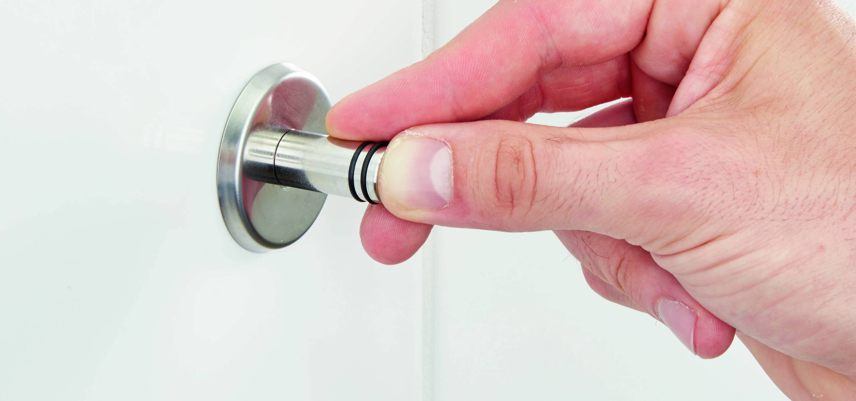 A hand turns a magnetic clasp button on a white surface.