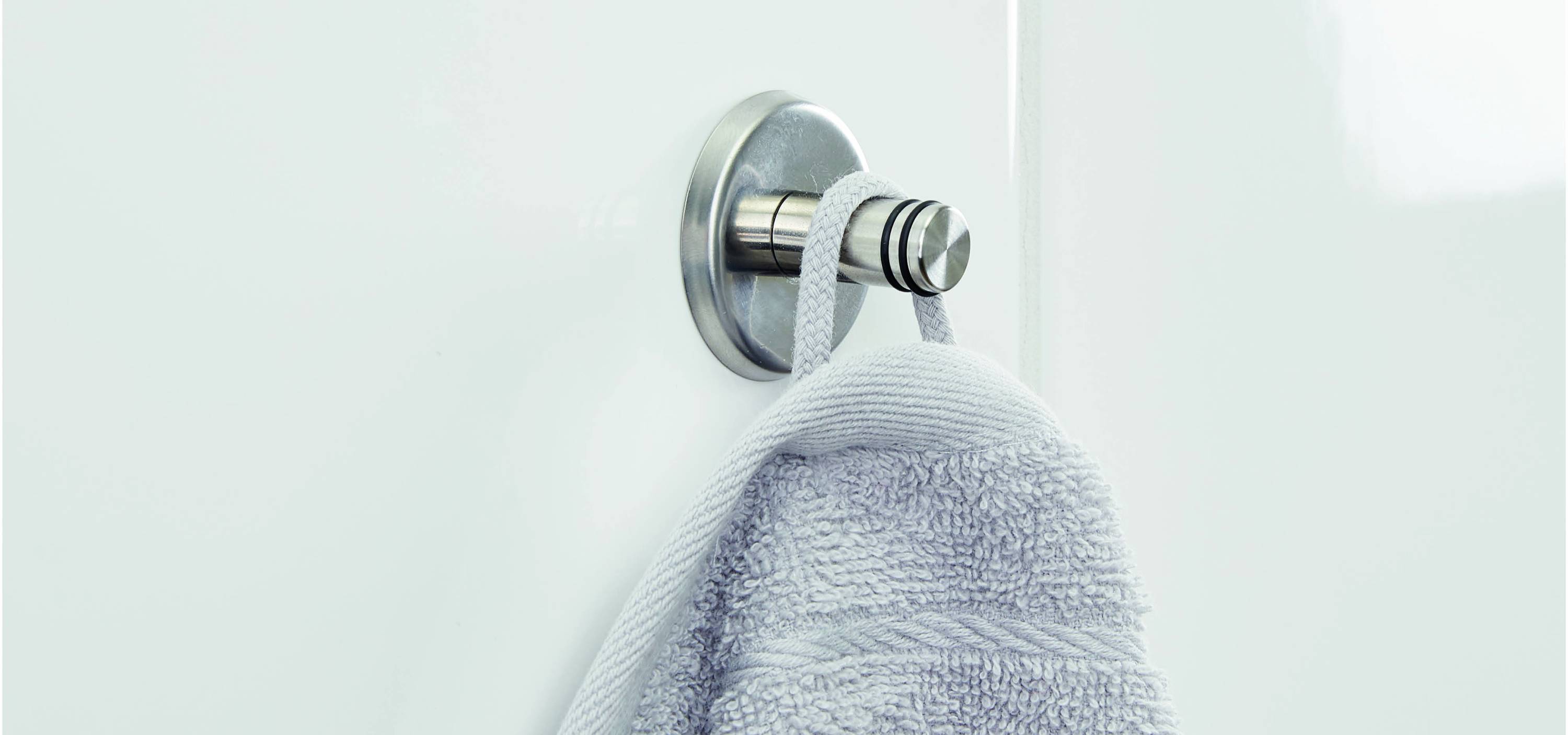 A grey towel hangs on a silver hook on a white wall.