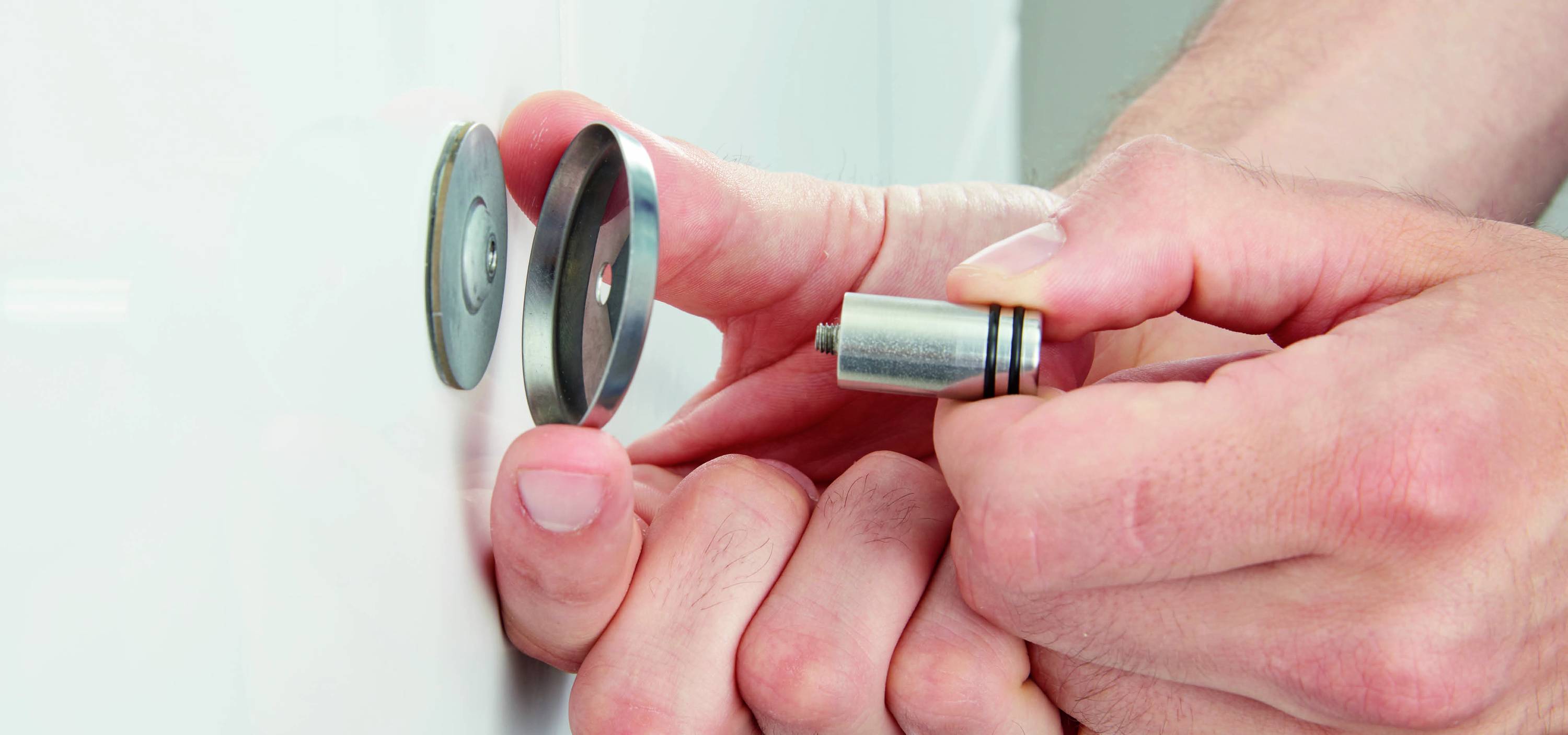 A person is mounting a magnetic catch hook on a white door, holding the magnetic cylinder in their hand.