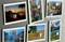 Six postcards featuring European landscapes and cities mounted on a wall. Depicting mountains, canals, and boats in picturesque scenes.