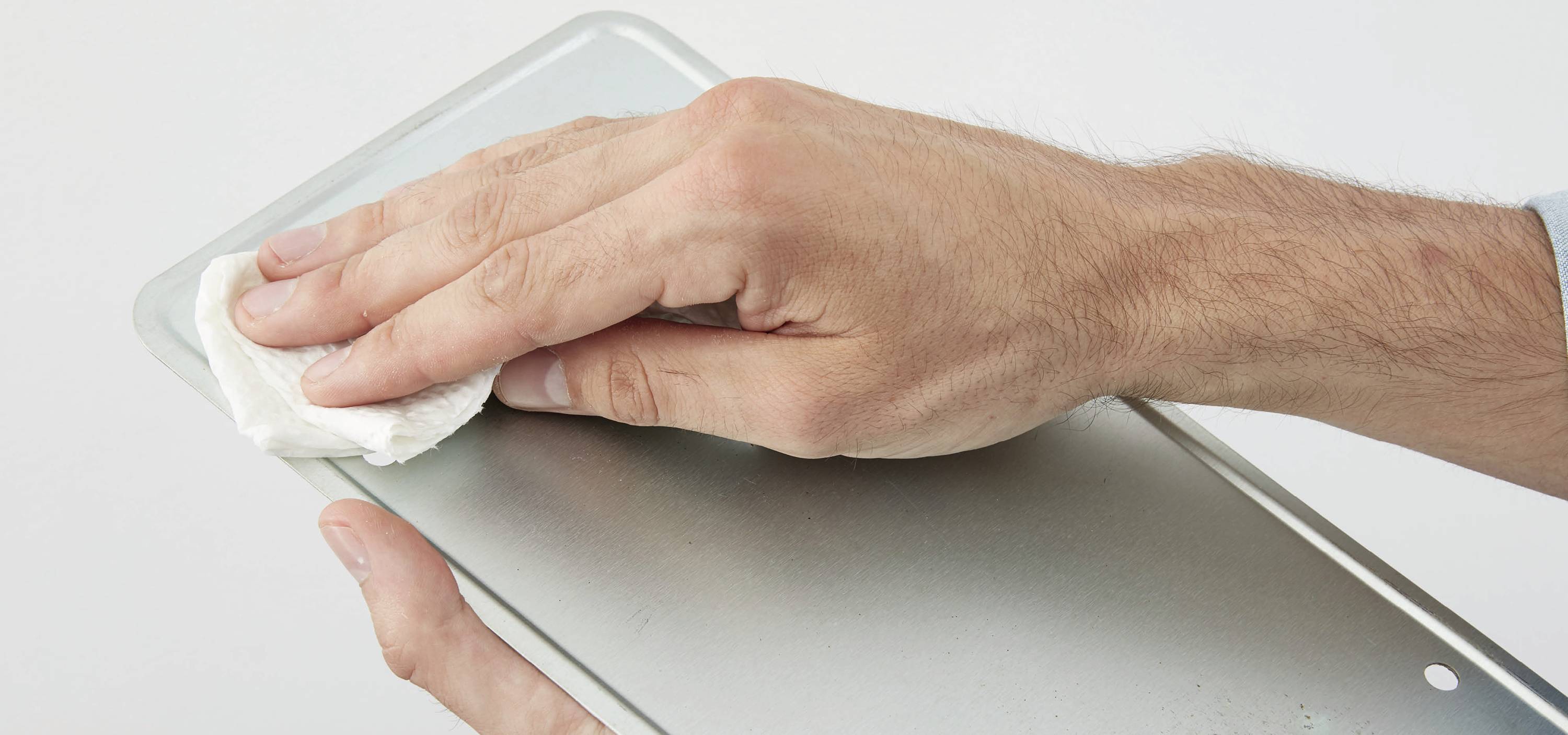 A hand is cleaning a metal surface with a white cloth.