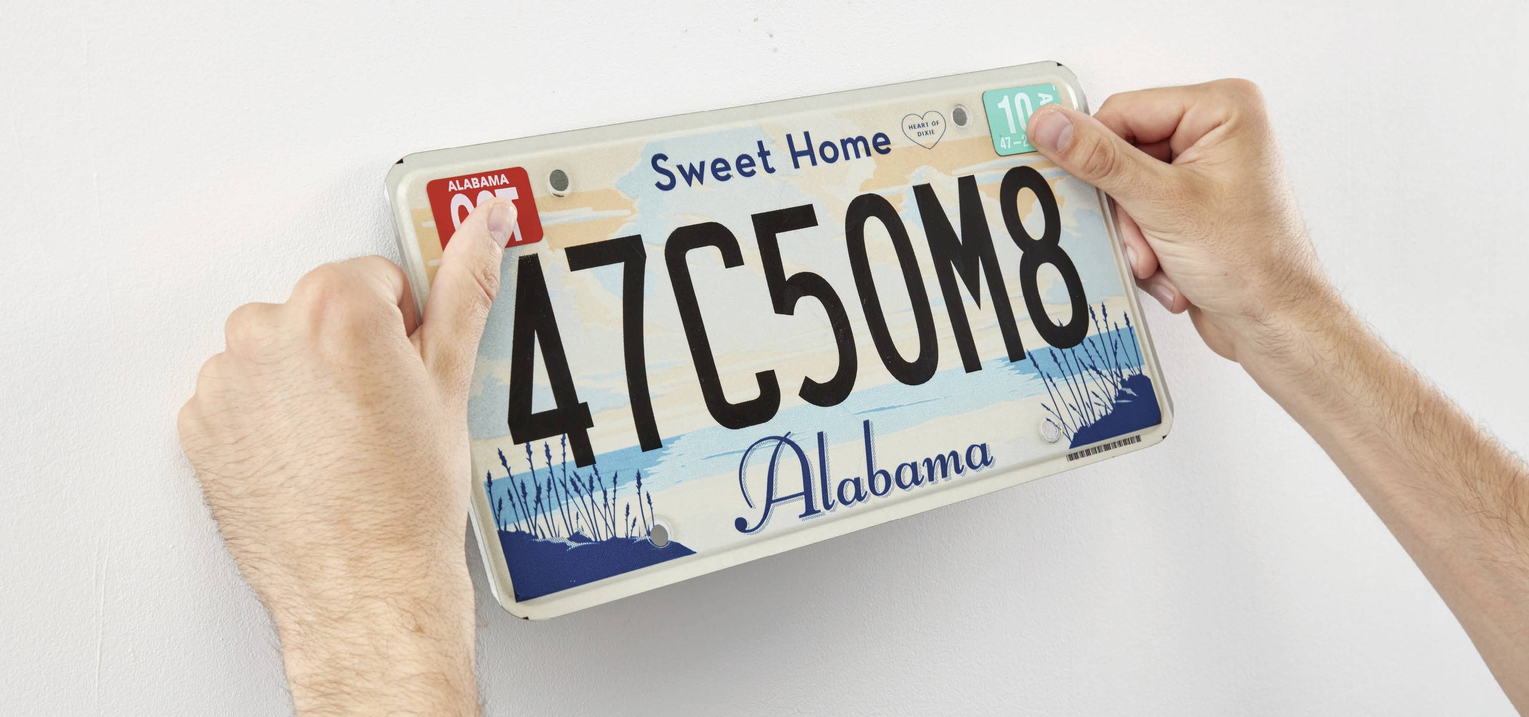 A person is mounting a number plate with the inscription 'Sweet Home Alabama' on a wall.