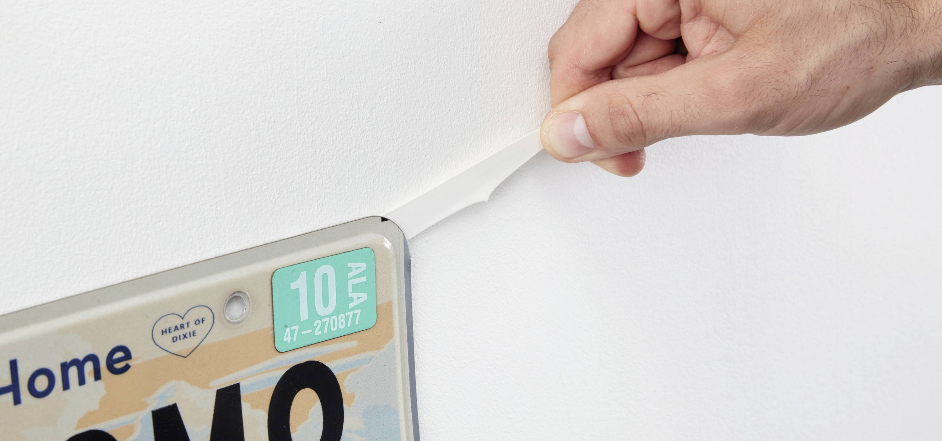 A hand peels a sticky strip from behind a number plate to remove it from the wall.