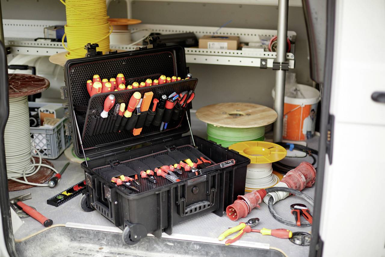 Toolbox open in the boot of a van, filled with screwdrivers and pliers. Cable reels and tools visible in the background.