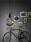 Bicycle against a grey wall with multiple framed pictures and a hanging light bulb displaying a spiral-shaped filament.