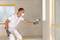 A man is spraying paint onto a wall in a room using a spray gun. He is wearing protective clothing and a mask.