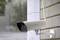 A surveillance camera is mounted on a wall and pointing outwards while it is raining.
