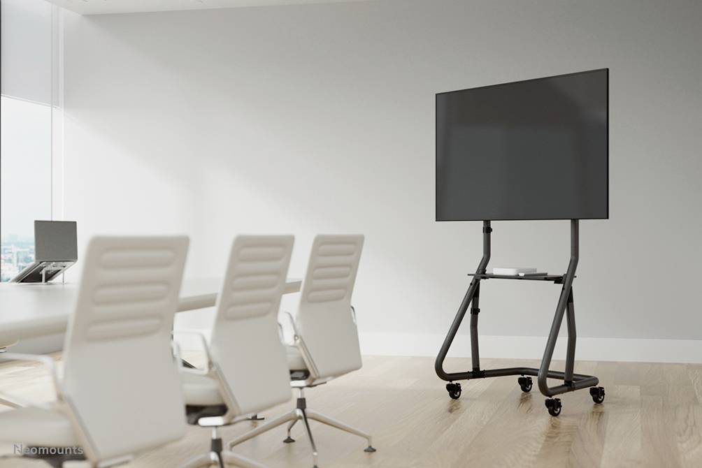 A modern conference room with a large screen on a mobile stand, surrounded by white, empty chairs around a table.