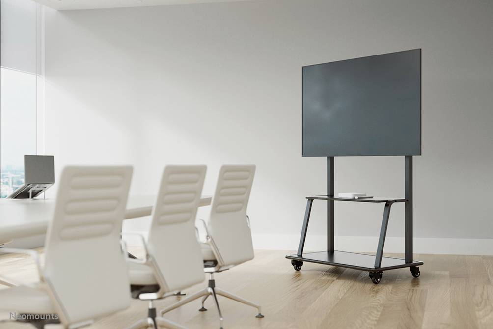 A conference room with a large screen on a mobile stand beside a table with chairs, suitable for presentations.