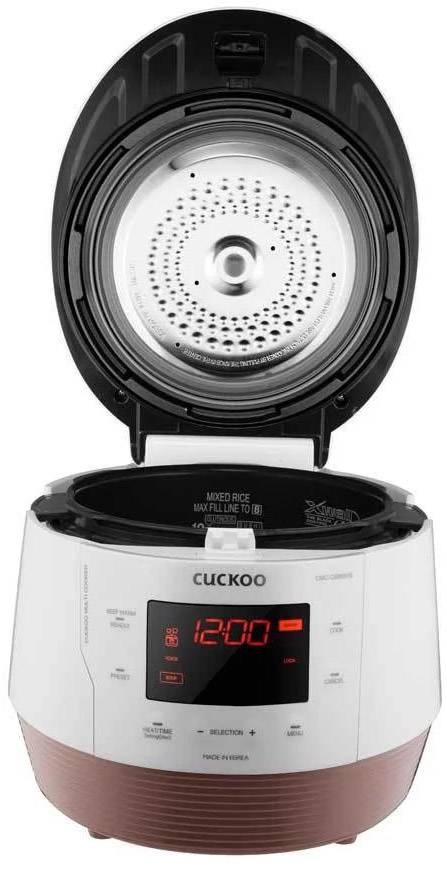 A white rice cooker with an open lid displays a digital screen with a red readout of '12:00'. The brand name 'CUCKOO' is visible.