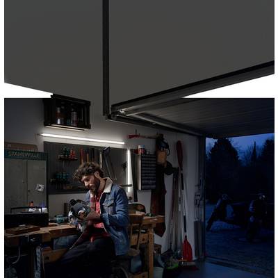 A man is sitting in a garage and working on a tool. The garage is dimly lit, and it is night outside.