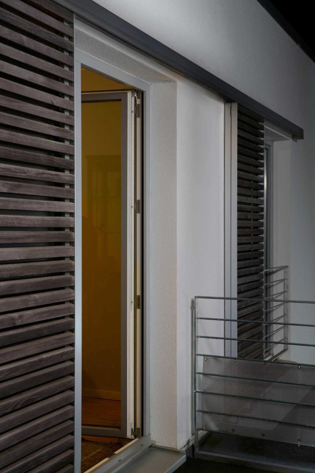 An open balcony door in a modern building, at night, with wooden panelling on the wall. A metal balustrade is visible.