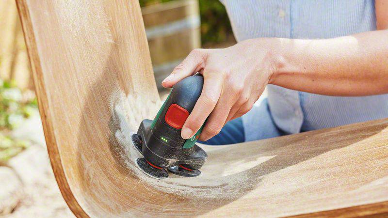 A person is sanding a wooden surface with an electric sanding tool to smooth it.