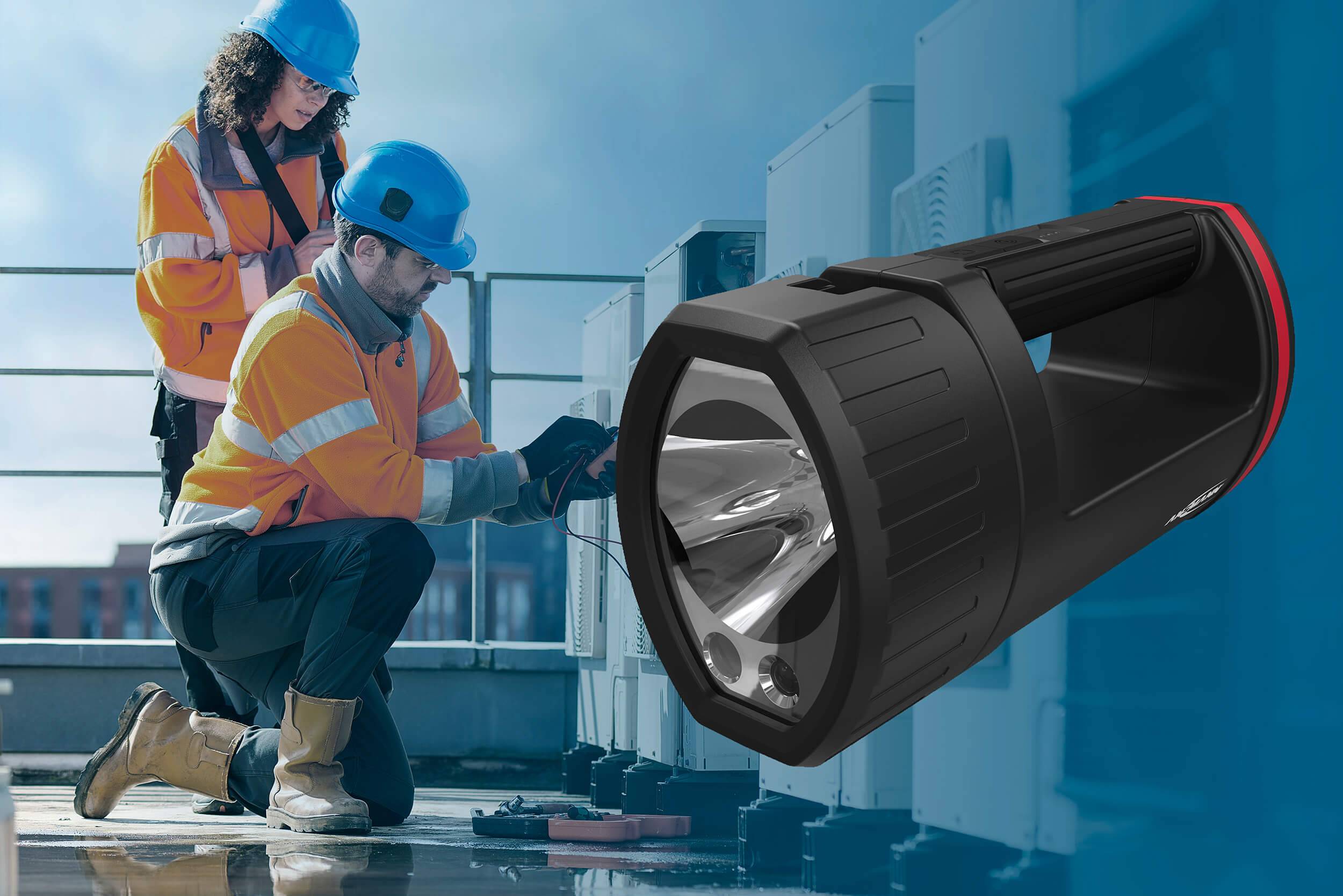 Two people in safety clothing are working on technical equipment on a roof. A large torch is pictured on the right side of the image.