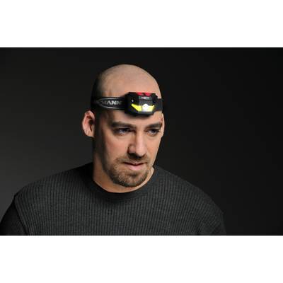 A person is wearing an activated head torch. They are wearing a dark grey jumper. The background is dark.