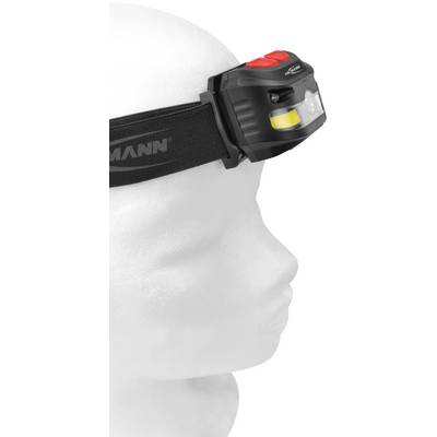 A model head is wearing a black head torch with a red button, viewed from the side. The torch is fastened to a black strap.