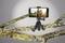 A smartphone on a flexible tripod, attached to a branch, displays an image of two people hiking in nature.