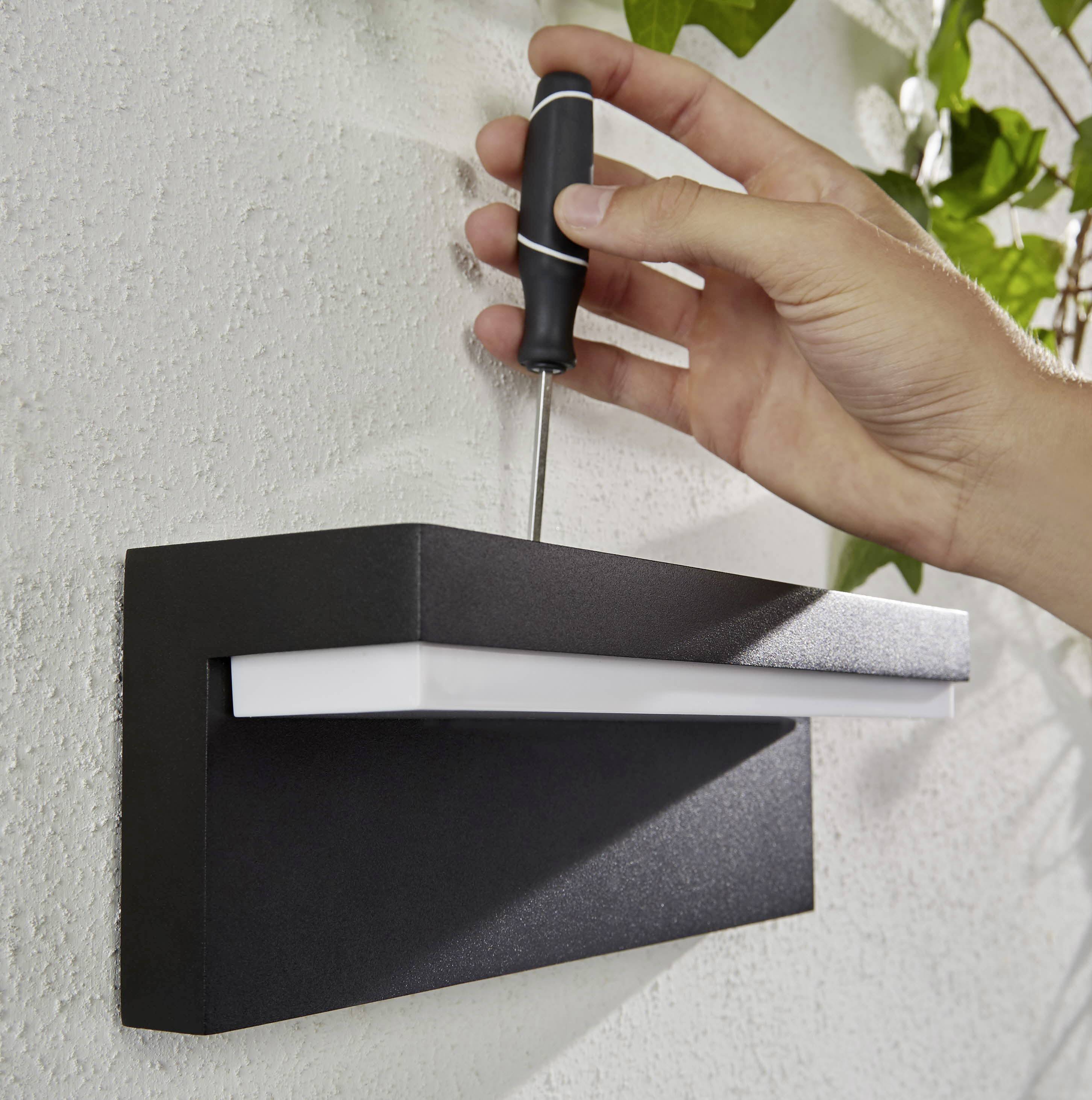 A hand is securing a black outdoor light to a wall using a screwdriver.