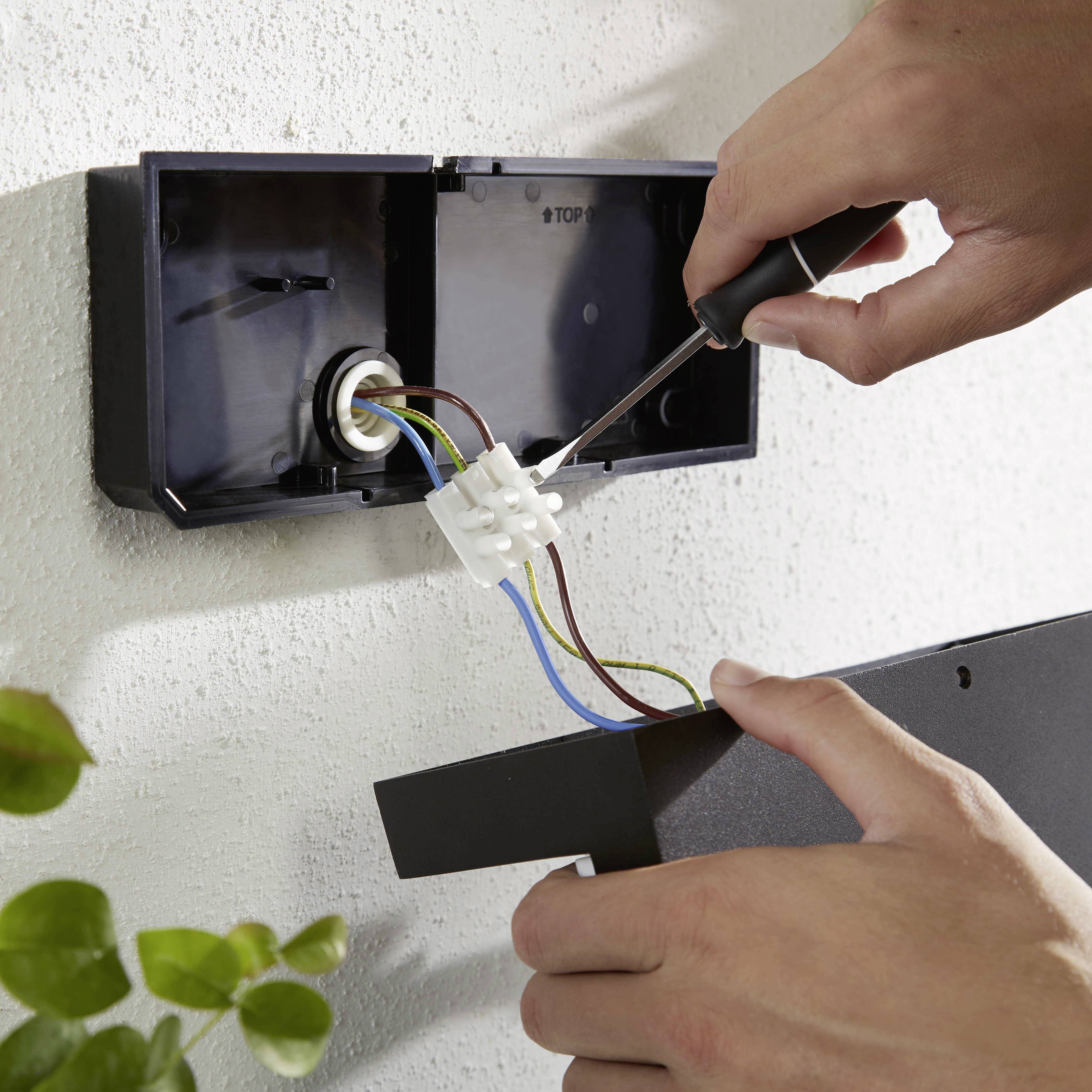 A person is installing a socket by connecting cables with a screwdriver in a junction box.
