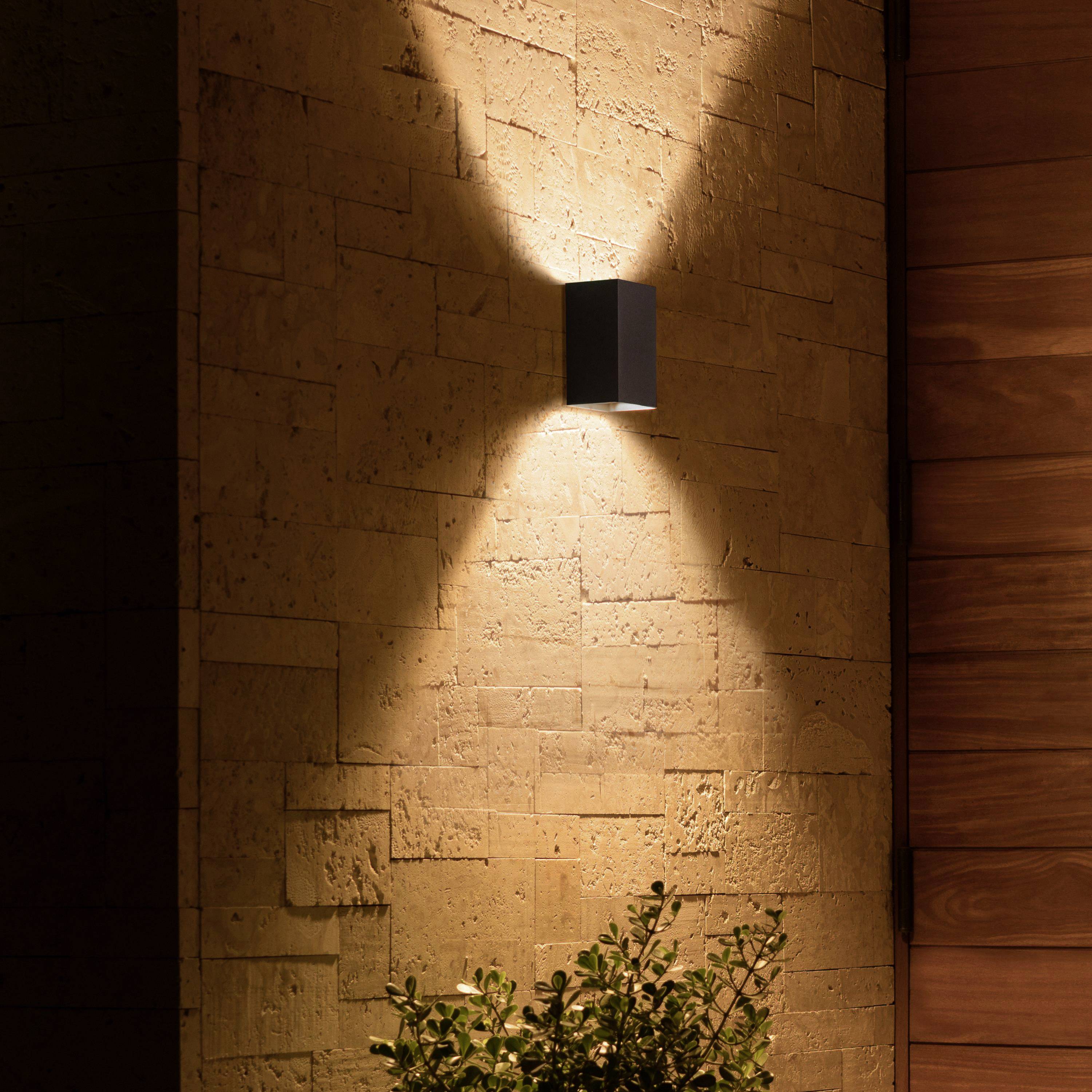 'Exterior wall light on a stone wall, creating diffused light. A small bush is situated at the bottom of the image.'