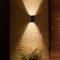'Exterior wall light on a stone wall, creating diffused light. A small bush is situated at the bottom of the image.'
