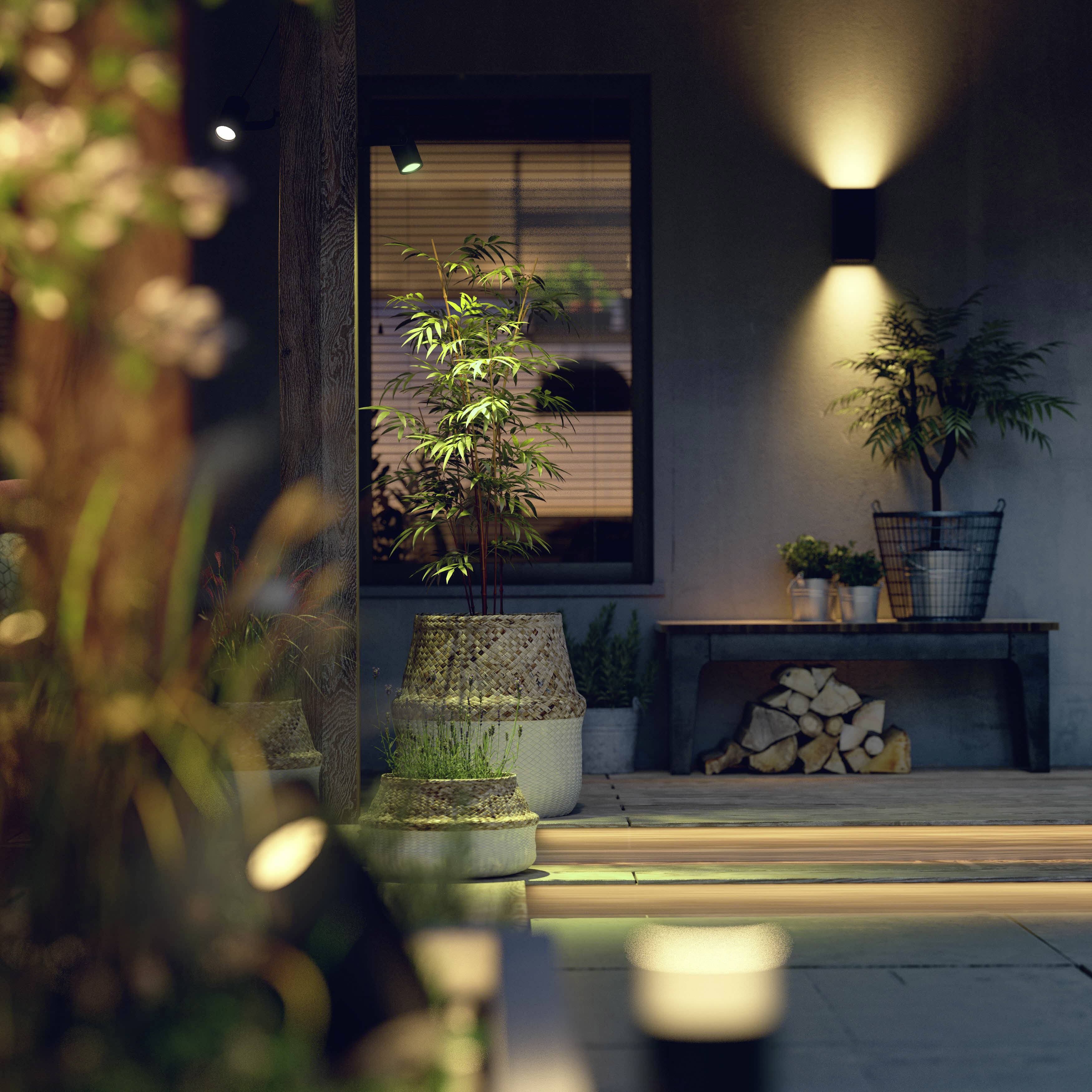 A terrace with potted plants, atmospheric lighting and a table with a stack of wood in the background.