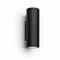 Black cylindrical wall light with upward and downward facing light sources, mounted on a white wall.