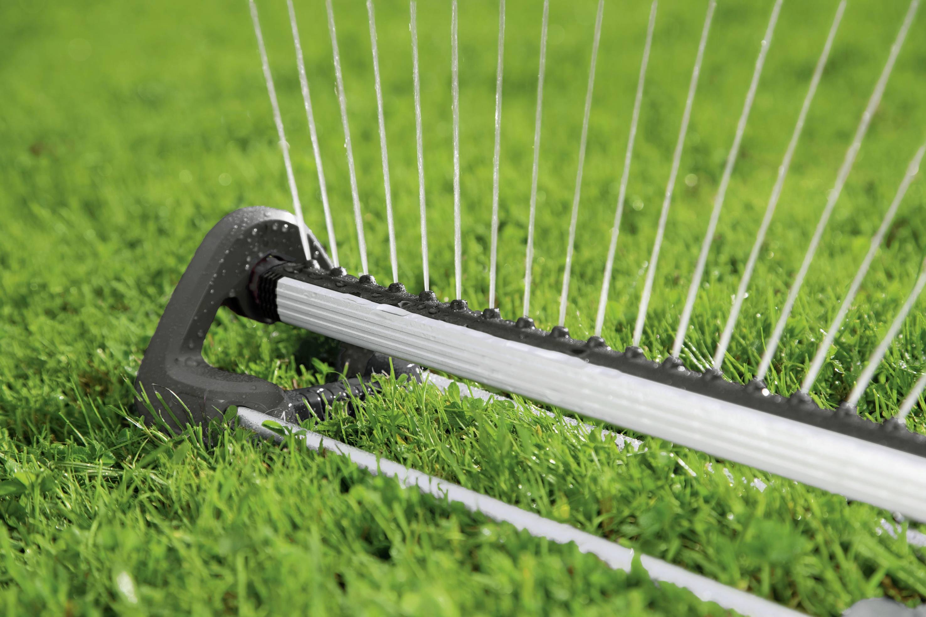A lawn sprinkler on green grass sprays parallel-running water jets. A close-up shows the details of the sprinkler system.