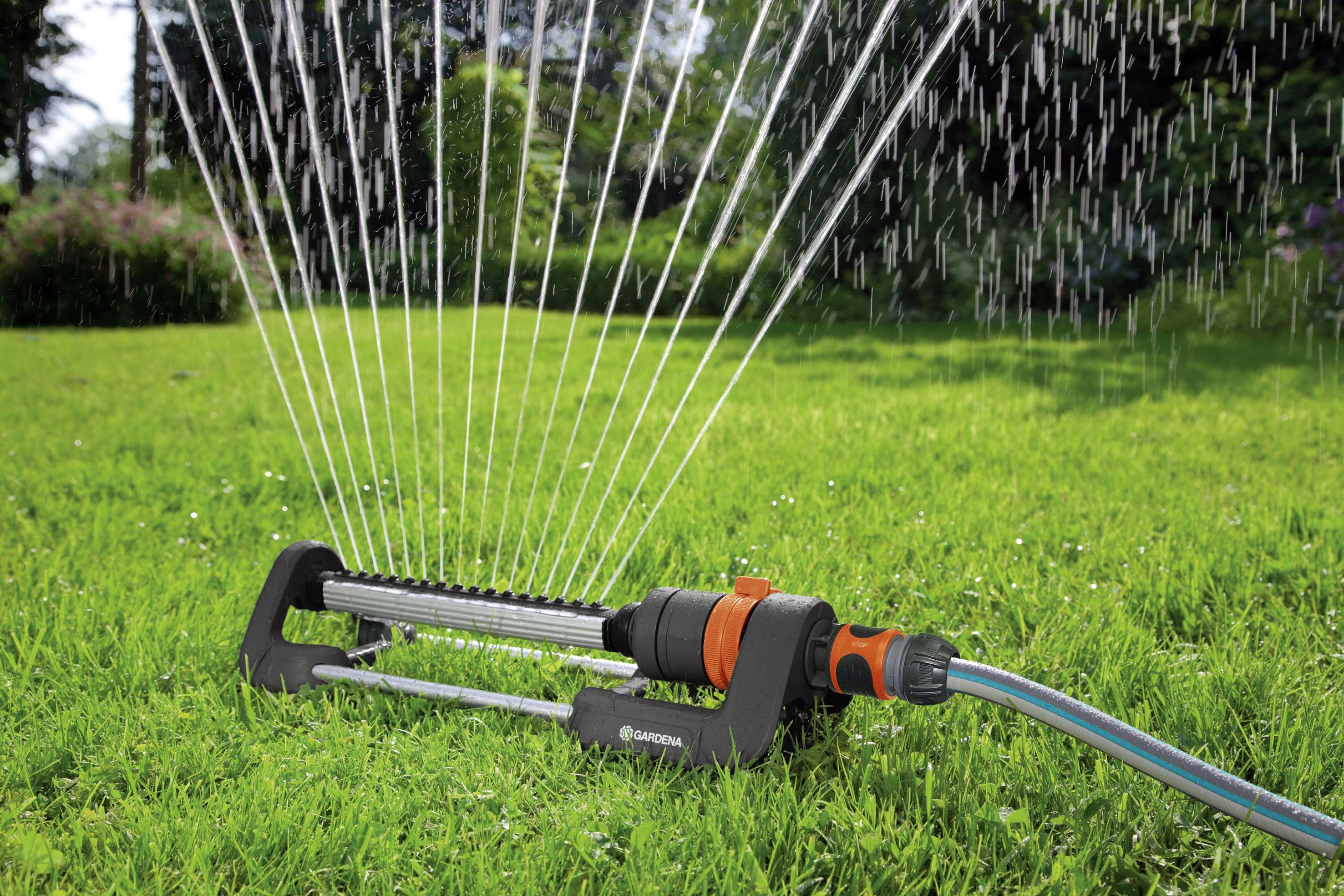 A lawn sprinkler is watering a green lawn evenly on a sunny day.