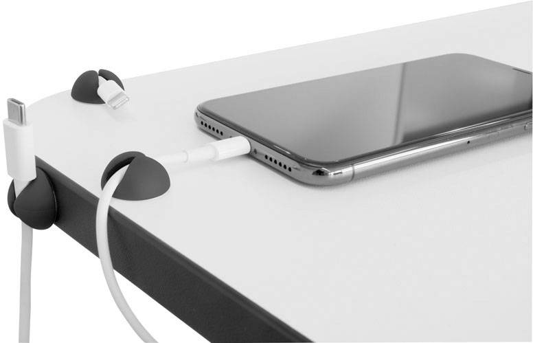 A smartphone is lying on a table. A white charging cable is connected to its port and is secured by cable holders.