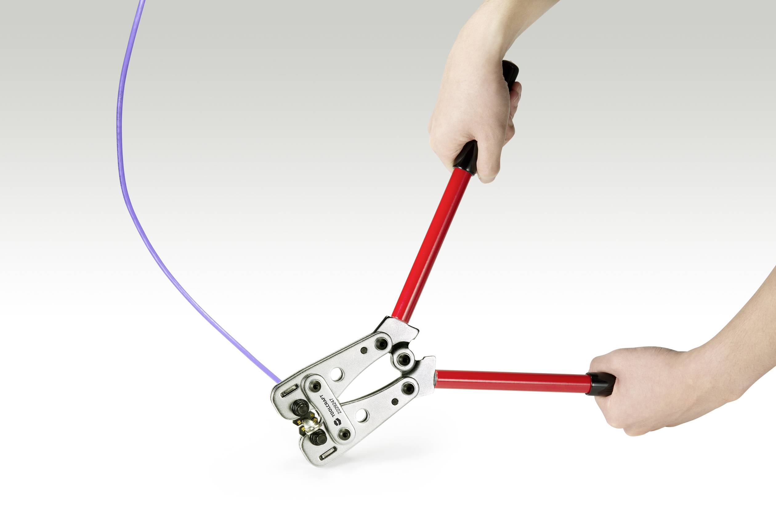Two hands operate a bolt cutter with red handles, cutting through a purple cable.