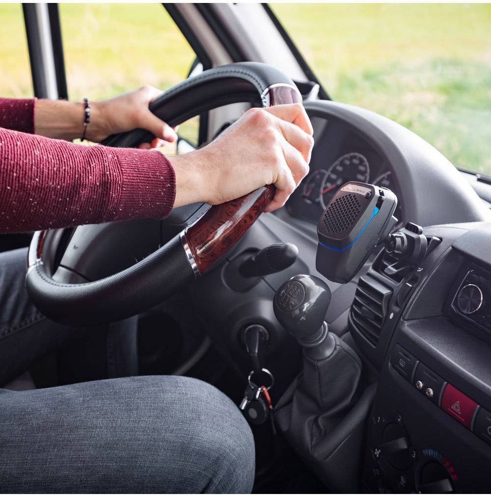 A person is driving a vehicle, gripping the steering wheel firmly. A radio is mounted on the dashboard.