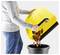 A person empties a yellow vacuum bin full of debris into a black trash can, demonstrating easy disposal.