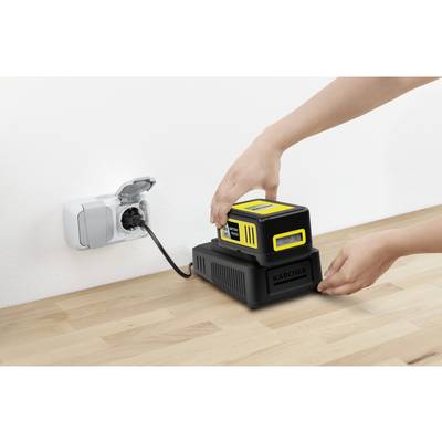 A person is charging a yellow battery with a black charging station that is connected to a power socket.