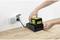 A person is charging a yellow battery with a black charging station that is connected to a power socket.