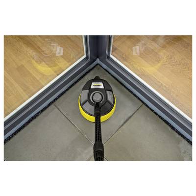 A floor cleaning device is shown cleaning a tile floor near the corner of a glass door, demonstrating its ability to clean edges effectively.