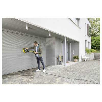 A person cleans a white garage door using a pressure washer on a paved driveway outside a modern house.